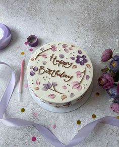 a birthday cake sitting on top of a table next to some purple ribbons and flowers