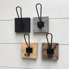 three square wooden pieces with black metal handles and hooks on each side, hanging from white wood planks