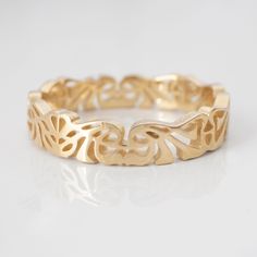 a gold ring with filigrees and leaves on the inside, sitting on a white surface