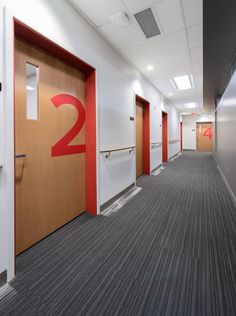 an empty hallway with red and white door numbers on the wall, and two doors leading to another room