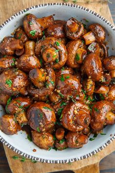 a white bowl filled with cooked mushrooms on top of a wooden cutting board and garnished with parsley