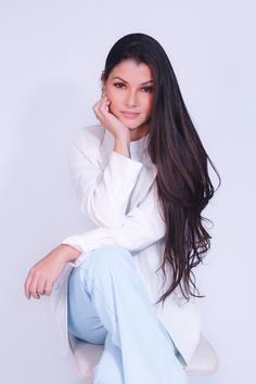 a woman sitting on top of a white chair with her hand under her chin and looking at the camera