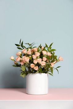 a white vase filled with lots of pink flowers on top of a table next to a blue wall