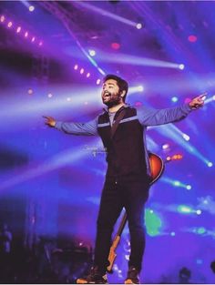 a man standing on top of a stage with his arms out in the air and lights behind him