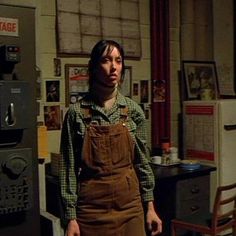 a woman in overalls standing next to a machine