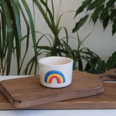 a cup with a rainbow painted on it sitting on top of a cutting board next to some plants