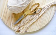 a pair of scissors sitting on top of a wooden cutting board next to some yarn