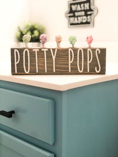 a wooden sign that says potty pops on top of a blue dresser in a bathroom