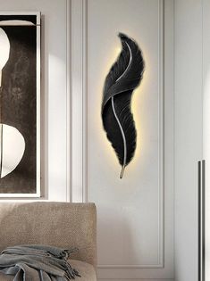 a black feather is hanging on the wall next to a white chair and light fixture