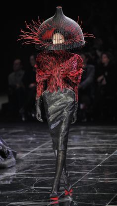 a woman in black and red is walking down the runway