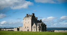 an old castle sitting on top of a lush green field next to the ocean with clouds in the sky