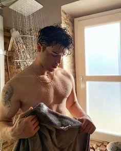 a shirtless man standing in front of a shower holding a towel and looking down