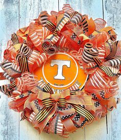 an orange and black wreath with the letter t on it is hanging on a wooden wall