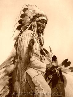 an old black and white photo of a native american man with feathers on his head