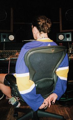 a woman sitting in an office chair with her back turned to the camera and looking at sound equipment