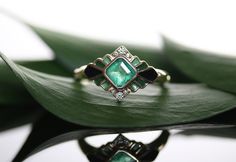 an emerald colored ring sitting on top of a green leaf with diamonds around the edges