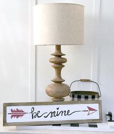 a lamp sitting on top of a table next to a sign that says be mine