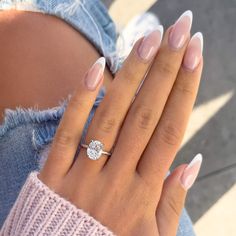 a woman's hand with a diamond ring on her left hand and a pink sweater