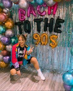 a woman sitting on the floor in front of balloons and streamers that say back to the 90's