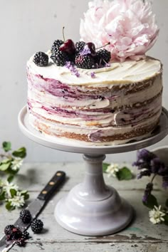 a layered cake with berries and cream frosting on a white pedestal next to flowers