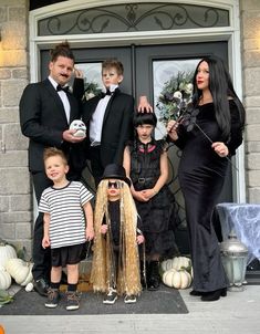 a family dressed up for halloween standing in front of a house with pumpkins and decorations