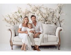 a man, woman and child sitting on a couch in front of a floral wall