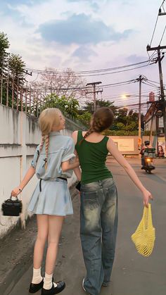 two young women walking down the street with their hands in each other's pockets