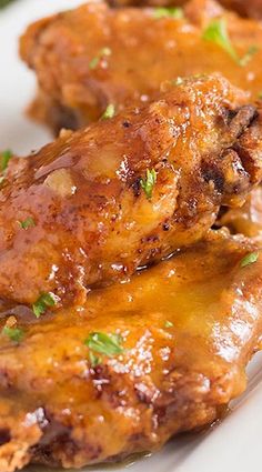 two pieces of chicken covered in gravy on a white plate with green garnish