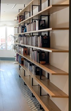 a bookshelf filled with lots of books on top of wooden shelves next to a window