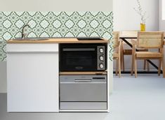 a kitchen with an oven, dishwasher and table next to the wall that has green tiles on it