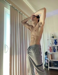 a shirtless man standing in front of a window with his hands on his head