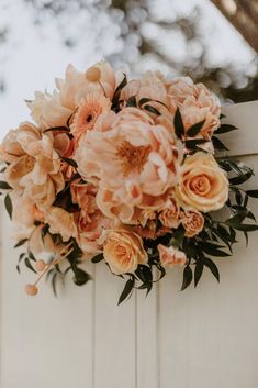 a bunch of flowers hanging from the side of a white fence with greenery on it