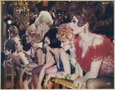 a group of women sitting next to each other in front of a christmas tree with lights