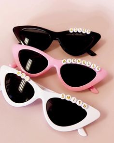 three pairs of sunglasses with personalized name stickers on the lenses and one pair is black, white, and pink