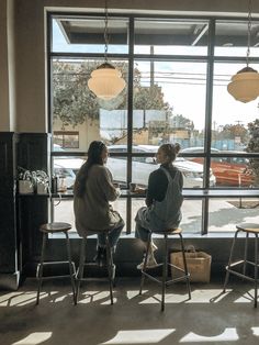 two women sitting at a table in front of a window looking out on the street