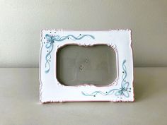 a white and pink frame with blue flowers on it, sitting on a table next to a wall