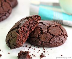 two chocolate cookies sitting next to each other on a white surface with one broken in half