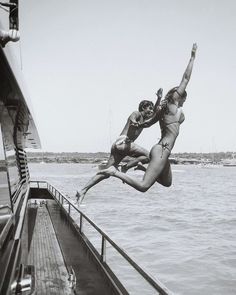 two women jumping off the side of a boat into the water while another woman watches