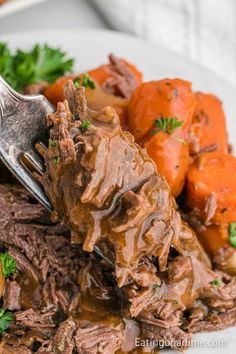 a fork full of beef and carrots on a white plate with parsley garnish