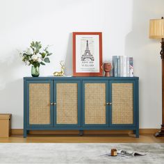 a blue cabinet with wicker doors in a living room next to a lamp and flowers