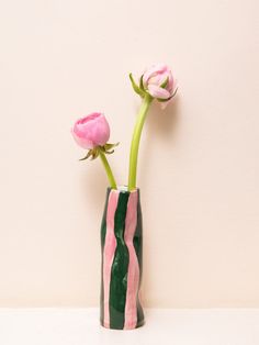 two pink flowers in a green vase on a white countertop against a beige wall