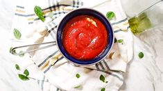 a blue bowl filled with red sauce on top of a white and green towel next to a bottle