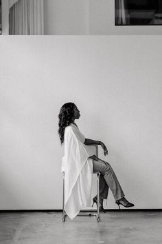 a black and white photo of a woman sitting on a chair in front of a wall