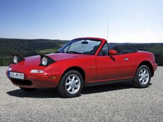 a red sports car parked on top of a gravel road