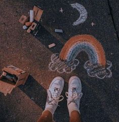 someone's feet standing on the sidewalk next to chalk drawings and other things in front of them