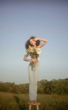 a woman standing on top of a wooden stool holding a bouquet of flowers in front of her face