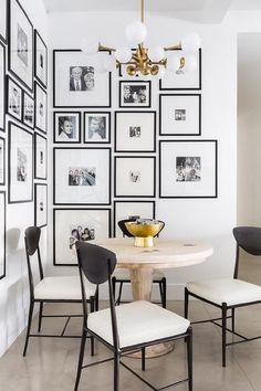 a white dining room with black and white pictures on the wall, two chairs and a round table