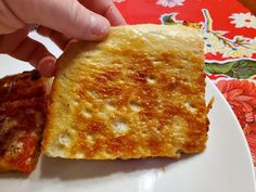 a person is holding up a piece of pizza on a white plate with red and floral table cloth