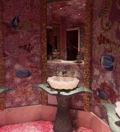 a bathroom with pink and green wallpaper has a pedestal sink in the center, under a mirror