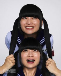 two women with black hair and bangs are smiling at the camera while one woman has her hair pulled back